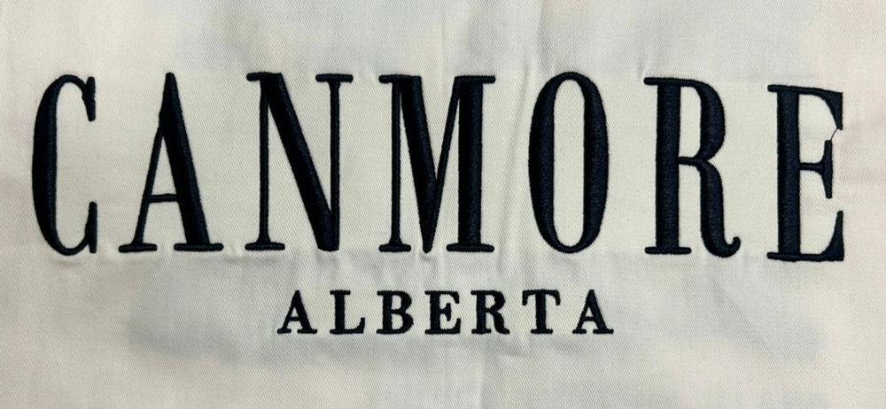 Direct flat embroidery reading Canmore Alberta on a cream garment